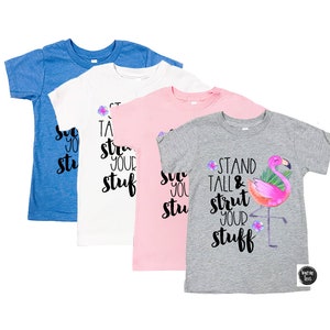 May include: Four t-shirts in different colours and designs. The shirts feature the text "Stand Tall & Strut Your Stuff" with a flamingo graphic. The shirts are available in blue, white, pink, and grey.