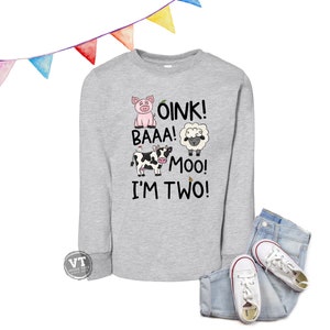 May include: A light gray long-sleeve sweatshirt with the text "OINK! BAAA! MOO! I'M TWO!" and illustrations of a pig, sheep, and cow. The sweatshirt is paired with blue jeans and white sneakers.