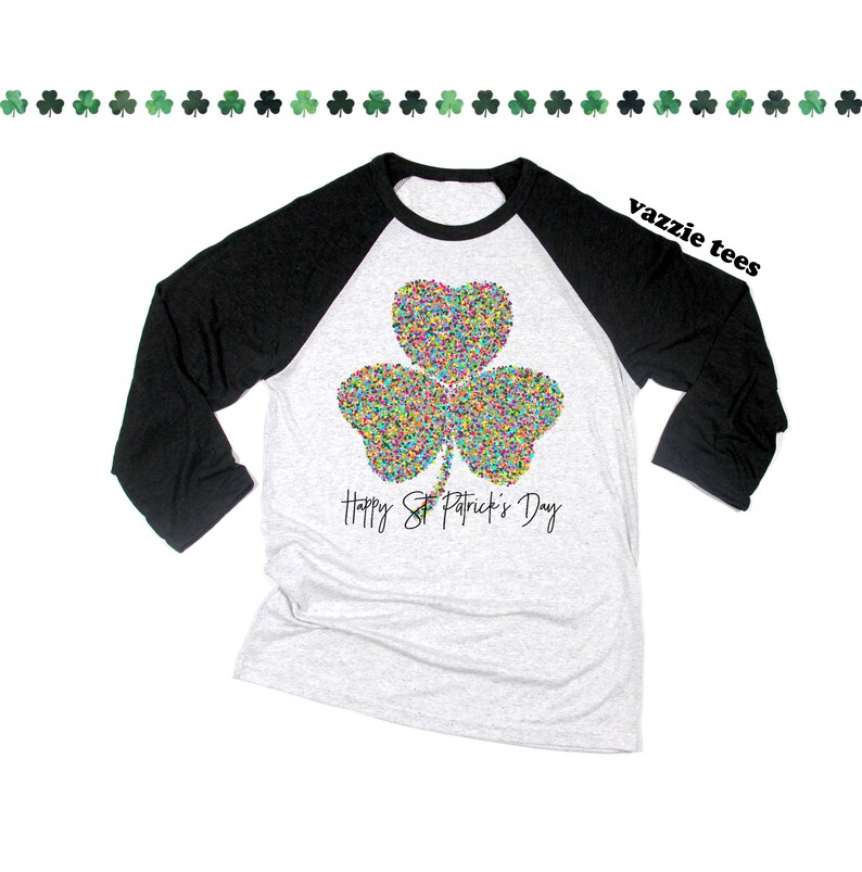 K&ouml;nnte beinhalten: Ein schwarz-wei&szlig;es Baseball-T-Shirt mit einem bunten Kleeblatt-Design und dem Text "Happy St. Patrick's Day".