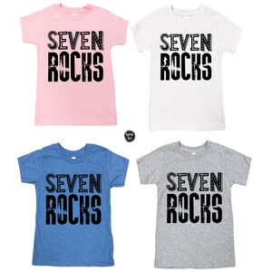 Puede incluir: Cuatro camisetas de diferentes colores con el texto "SEVEN ROCKS" impreso en negro en la parte delantera. Las camisetas son rosa, blanca, azul y gris.