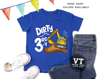 May include: A royal blue short-sleeve t-shirt featuring a yellow excavator graphic, a pile of brown dirt, and the white text "DIRTY 3RD-Y". The shirt is displayed with a pair of blue denim jeans and white canvas sneakers, accented by colorful bunting.