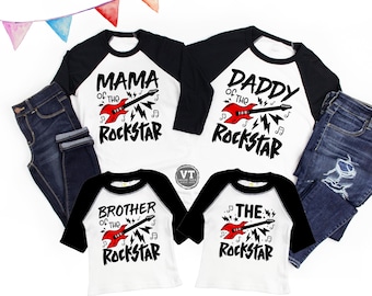 May include: A set of four white t-shirts with black sleeves. The shirts feature a red electric guitar graphic and text that reads "Mama of the Rockstar", "Daddy of the Rockstar", "Brother of the Rockstar", and "The Rockstar".