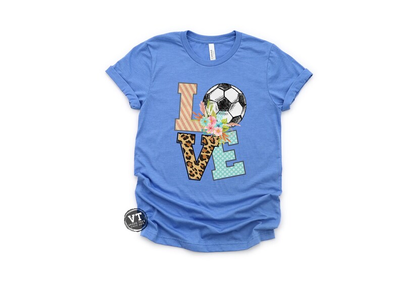 May include: A blue t-shirt with the word "LOVE" spelled out in colorful patterned letters. A soccer ball is on top of the "O" with flowers around it.