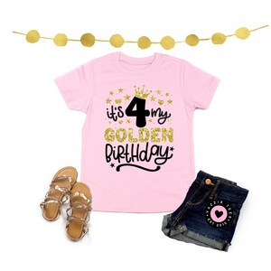 May include: A pink t-shirt with the text "it's my 4 GOLDEN BIRTHDAY" in gold glitter and black lettering. The image also includes denim shorts, gold sandals, and a gold star garland.