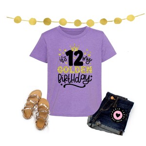 May include: A lilac-colored t-shirt with the text "it's my GOLDEN Birthday 12" in gold glitter and black script, paired with denim shorts and gold sandals. A festive birthday outfit.