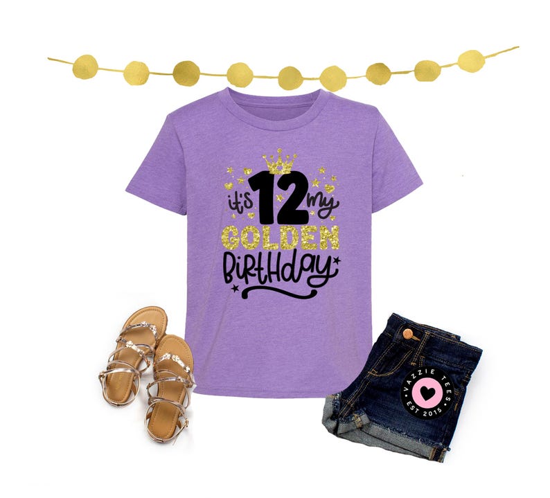 May include: A lilac-colored t-shirt with the text "it's my GOLDEN Birthday 12" in gold glitter and black script, paired with denim shorts and gold sandals. A festive birthday outfit.