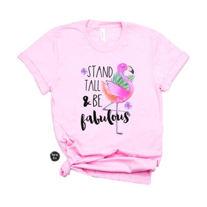 May include: Pink t-shirt featuring a flamingo graphic and the text "Stand Tall & Be Fabulous".