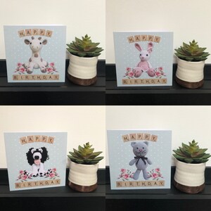 Peut inclure: Quatre cartes de vœux faites à la main avec des figurines d'animaux en crochet. Chaque carte présente un animal différent : une girafe, un lapin, un chien et un ours. Les cartes sont décorées de roses roses et d'un fond bleu à pois blancs. Les mots « JOYEUX ANNIVERSAIRE » sont orthographiés à l'aide de jetons de lettres.