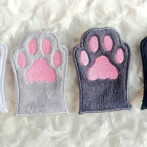 Könnte beinhalten: Vier Plüsch-Katzenpfoten-Patches in Weiß, Grau, Dunkelgrau und Schwarz mit rosa Pfotenballen.