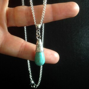 Puede incluir: Un collar de cadena de plata con un colgante de l&aacute;grima turquesa. El colgante tiene una tapa de plata con un dise&ntilde;o ornamentado.