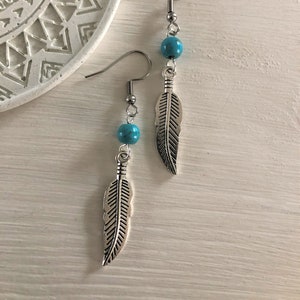 May include: A pair of silver feather earrings with turquoise beads. The earrings have a simple design and are perfect for everyday wear.