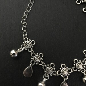 May include: Silver anklet featuring a chain and decorative charms. The charms include small bells and circular designs.