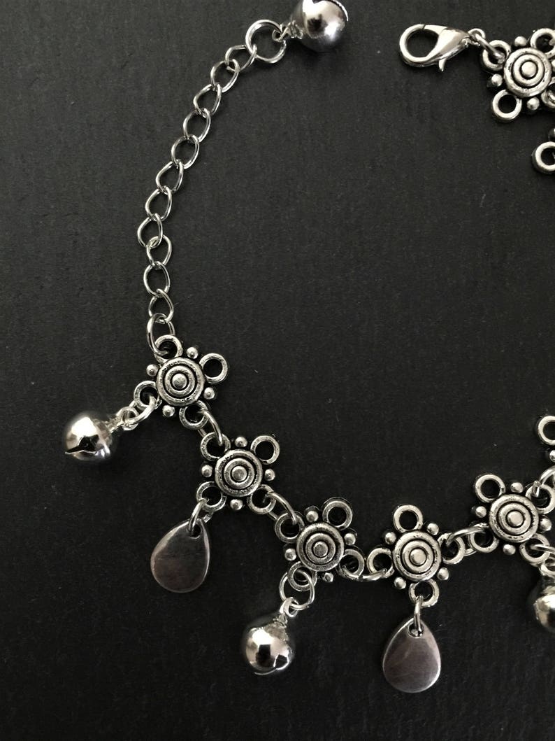 May include: Silver anklet featuring a chain and decorative charms. The charms include small bells and circular designs.