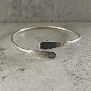 May include: A silver-coloured open cuff bracelet. The bracelet has a hammered texture on the flared ends. The bracelet is a simple, elegant design.