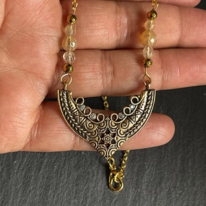May include: Gold necklace with a detailed ornate pendant and clear faceted beads.