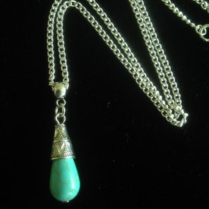 Puede incluir: Un collar de cadena de plata con un colgante de l&aacute;grima turquesa. El colgante tiene una tapa de plata con un dise&ntilde;o ornamentado.