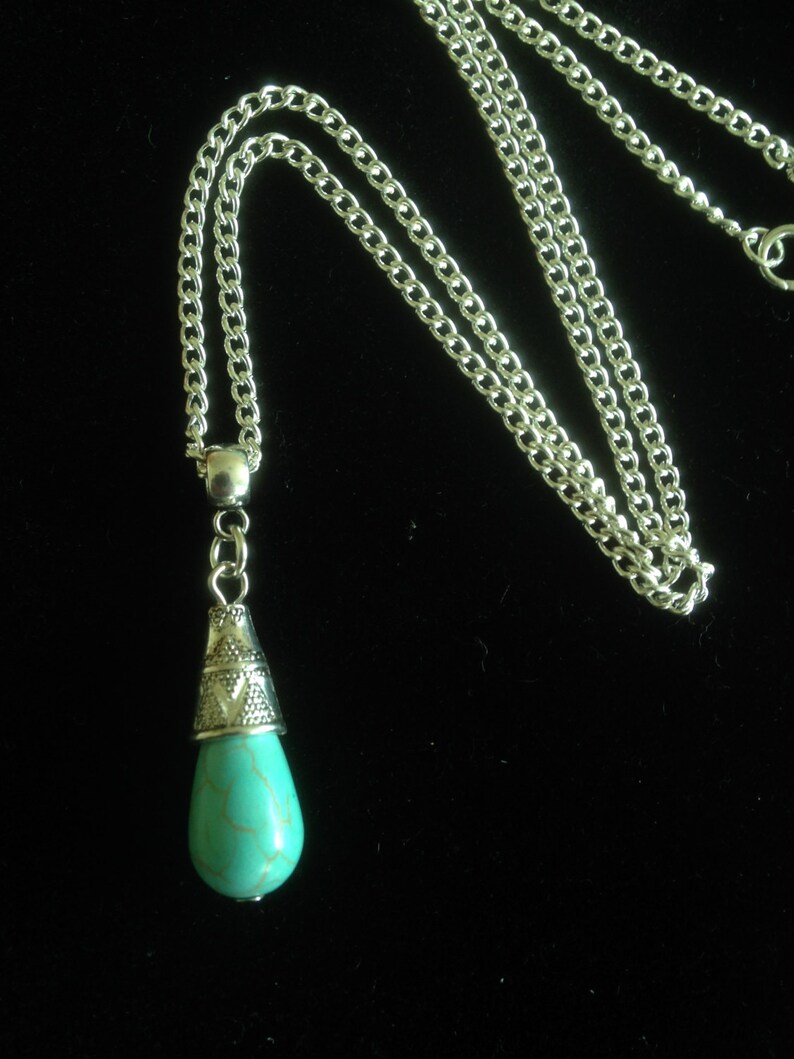 Puede incluir: Un collar de cadena de plata con un colgante de l&aacute;grima turquesa. El colgante tiene una tapa de plata con un dise&ntilde;o ornamentado.