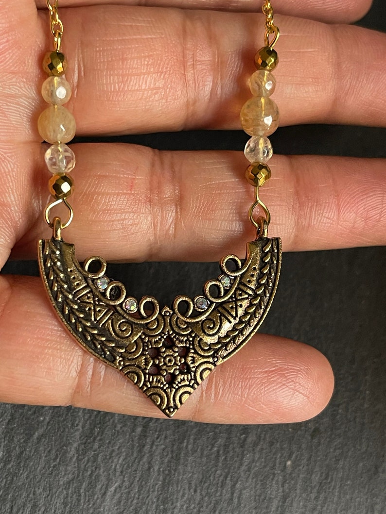 May include: A gold necklace with a detailed, ornate pendant and clear faceted beads. The pendant is shaped like a crescent moon and has a delicate, intricate design.