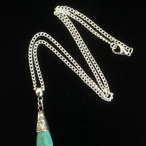 Puede incluir: Un collar de cadena de plata con un colgante de l&aacute;grima turquesa. El colgante tiene una tapa de plata con un dise&ntilde;o ornamentado.
