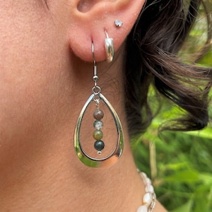 May include: Silver teardrop earrings with a row of green, brown and white gemstone beads hanging from the centre.