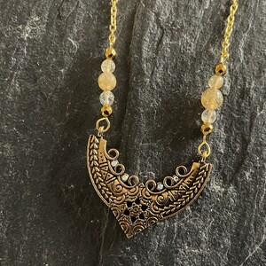 May include: A gold necklace with a detailed, ornate pendant and clear, faceted beads.