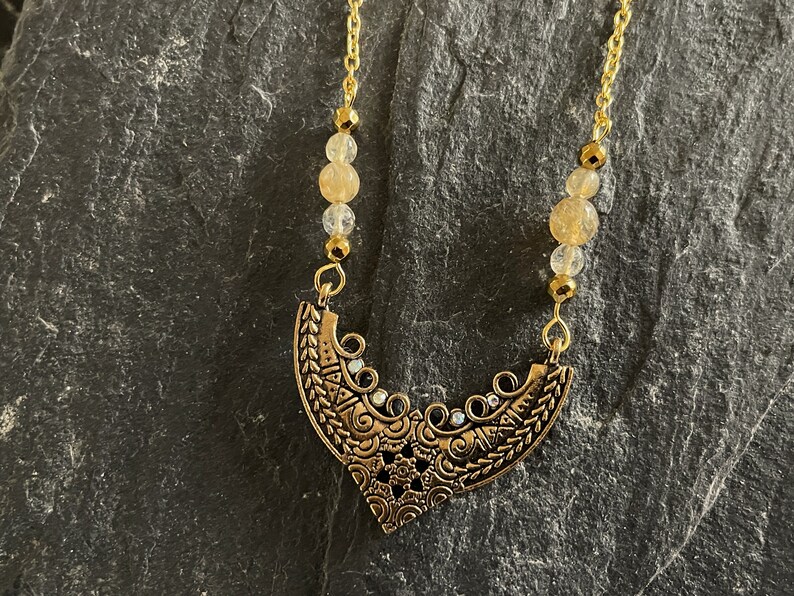 May include: A gold necklace with a detailed, ornate pendant and clear, faceted beads.