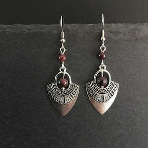 May include: Silver earrings with a geometric design and burgundy beads.