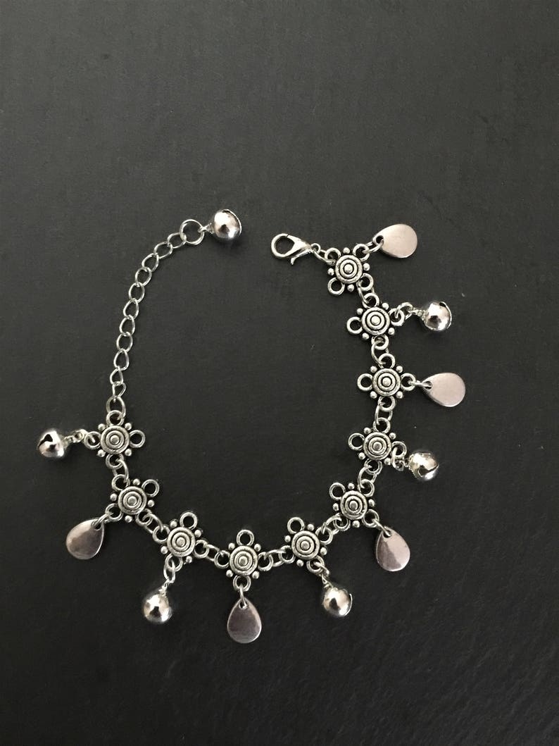 May include: Silver anklet with a chain design and decorative charms. The charms include small bells and teardrop shapes.