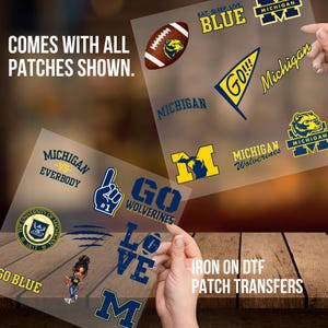 Puede incluir: Un conjunto de parches termoadhesivos con el logotipo de los Wolverines de la Universidad de Michigan, la mascota y otros diseños. Los parches están en una hoja transparente e incluyen el texto "Go Wolverines", "Michigan vs. Everybody", "Go Blue", "Eat. Sleep. Live. Blue" y "Love".