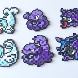 Op de afbeelding: Zes kleurrijke pixel art-figuren gemaakt met Perler-kraaltjes. De figuren zijn een lichtblauw en wit figuur, een paars figuur, een paars figuur met een rode mond, een paars figuur met een wit oog, een paars figuur met een wit oog en een blauw en paars figuur.