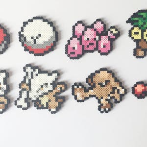 Può includere: Una collezione di otto personaggi Pokémon in pixel art realizzati con perline colorate. I personaggi includono Bulbasaur, Squirtle, Charmander, Pidgey, Pikachu, Eevee e altri due Pokémon.