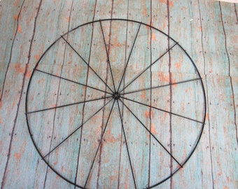 May include: A black metal hoop with spokes radiating from the center. The hoop is circular and has a rustic, aged look.