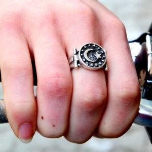 Könnte beinhalten: Ein silberner Ring mit einem Halbmond- und Stern-Design, umgeben von kleinen dekorativen Elementen. Der Ring wird an einem Finger getragen und zeigt seine detaillierte Handwerkskunst und symbolische Bildsprache.