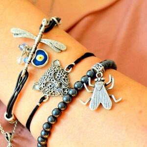 Könnte beinhalten: Ein Set aus vier Armbändern mit verschiedenen Anhängern. Ein Armband hat einen Libellenanhänger, ein anderes einen blauen bösen Blick-Anhänger, ein drittes einen Leopardenanhänger und das vierte einen Fliegenanhänger.