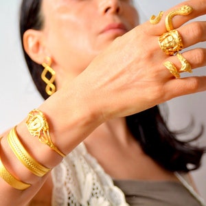 May include: A collection of gold-toned jewelry, including rings with snake and floral designs, a bracelet with a floral centerpiece, and multiple bangles. The earrings are a simple, yet elegant, infinity loop design.