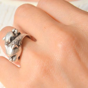 May include: A silver-toned ring featuring a detailed ram's head design. The ring has a textured finish and is worn on a finger. The ram's head is the focal point, with intricate detailing on the horns and face.