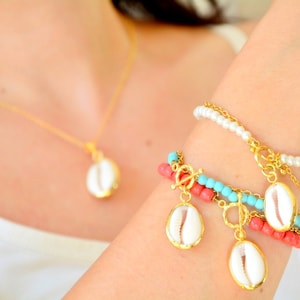 May include: A gold-toned necklace with a single white cowrie shell pendant and a multi-strand bracelet featuring white pearls, turquoise beads, coral-colored beads, gold chains, and three dangling white cowrie shell charms with gold-toned rims.