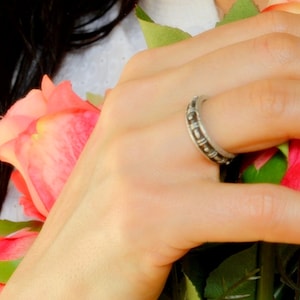Peut inclure: Une bague en argent avec un motif texturé, portée sur un doigt entouré de roses roses.