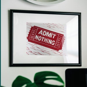 May include: A framed print of a red ticket with white text that reads "ADMIT NOTHING". The ticket is on a white background with a distressed, cracked paint effect.
