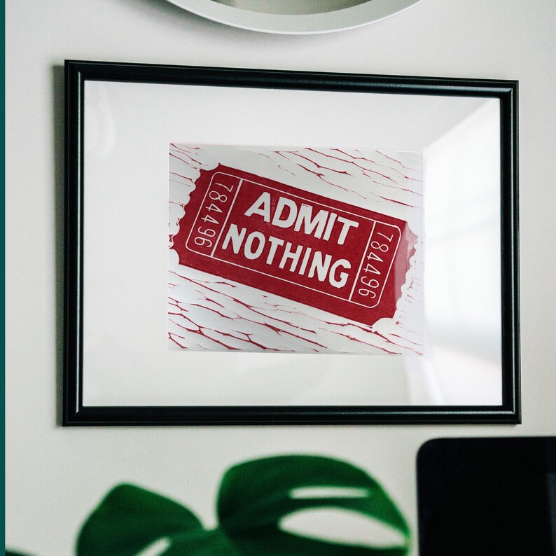 May include: A framed print of a red ticket with white text that reads "ADMIT NOTHING". The ticket is on a white background with a distressed, cracked paint effect.