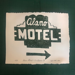 Puede incluir: Una impresión en blanco y negro de un letrero de motel vintage que dice "Alamo Motel - Los Alamos, CA". El letrero es de estilo retro con un esquema de color verde y blanco. La impresión está numerada 2/150 y firmada "Bytth 2022".