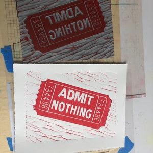 May include: A red and white ticket with the text "ADMIT NOTHING" and the number "784496" printed on it. The ticket is printed on a textured surface.
