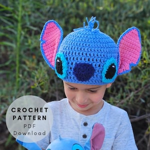 May include: A blue crochet hat with pink ears, black eyes, and a dark blue nose, resembling a cartoon character. The hat is worn by a child. The image includes the text "CROCHET PATTERN PDF Download".