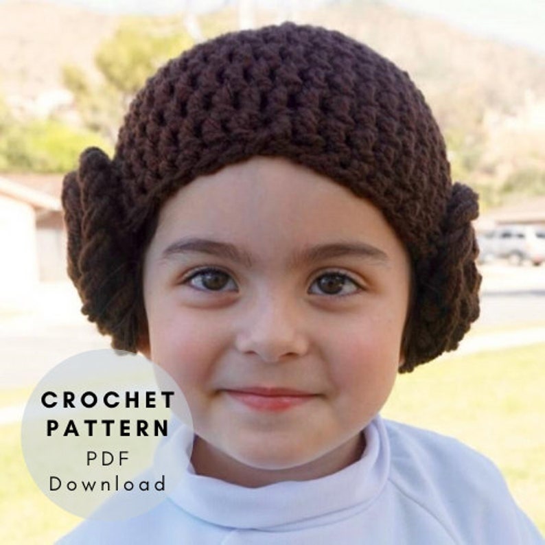 May include: A brown crochet hat with a bun on the side. The hat is worn by a child with a white shirt. The text "CROCHET PATTERN PDF DOWNLOAD" is on a white circle.