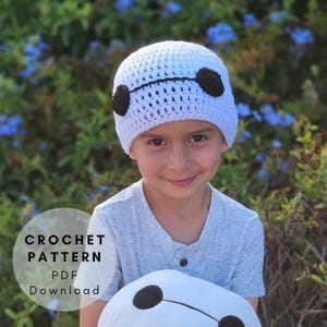 May include: A white crocheted hat with black accents, resembling a cartoon character, is worn by a child. The hat is paired with a light blue shirt. The image includes the text "CROCHET PATTERN PDF Download."