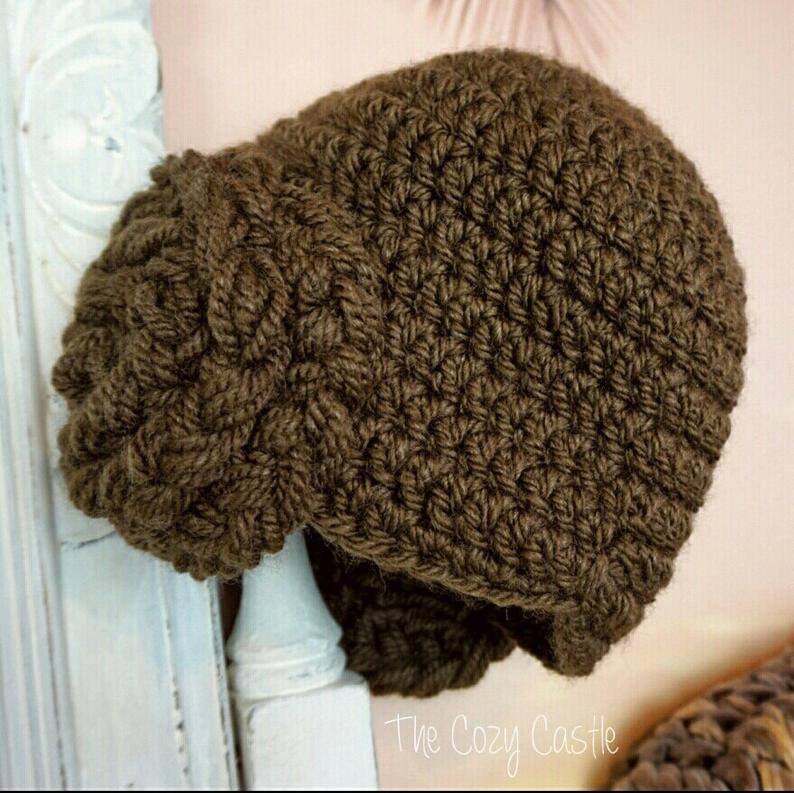 May include: A brown crocheted beanie with a unique braided design. The beanie is made with a soft, textured yarn and has a slouchy fit.