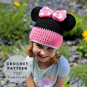 Puede incluir: Un gorro de ganchillo negro, rosa y blanco con orejas grandes y un lazo. El gorro lo lleva una persona. El texto "CROCHET PATTERN PDF Download" está en un círculo blanco en la esquina inferior izquierda.