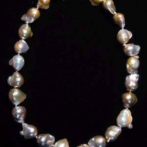May include: A necklace of irregularly shaped, lustrous pearls in shades of gold, silver, and green. The pearls are strung together with a delicate silver clasp. The necklace is displayed against a black background.