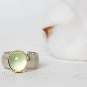 May include: A silver ring with a green gemstone set in a gold bezel. The ring has a textured band.