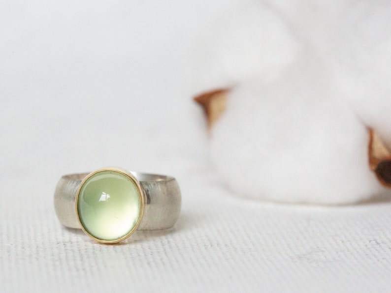 May include: A silver ring with a green gemstone set in a gold bezel. The ring has a textured band.